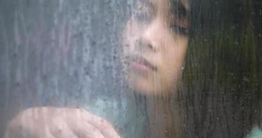 primer plano, joven asiática triste mirando por la ventana en un día lluvioso. concepto de depresión. video