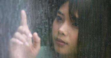 close-up tiro, asiática triste jovem olhando pela janela em dia chuvoso. conceito de depressão. video
