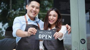 Happy restaurant owners are standing and holding sign open business. video