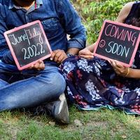 Indian couple posing for maternity baby shoot. The couple is posing in a lawn with green grass and the woman is falunting her baby bump in Lodhi Garden in New Delhi, India photo