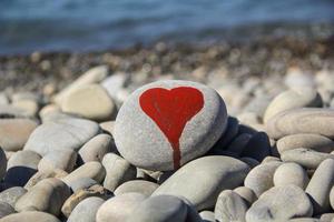 stone heart painted with a red paint marker on the pebble as a gift for Saint Valentine day on the pebble background. photo