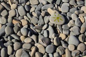 Bright sun painted on pebble. Pebbles background. photo