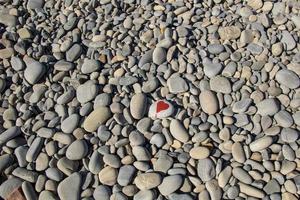 stone heart painted with a red paint marker on the pebble as a gift for Saint Valentine day on the pebble background. photo