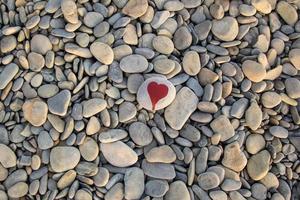 stone heart painted with a red paint marker on the pebble as a gift for Saint Valentine day on the pebble background. photo