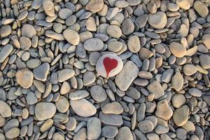 stone heart painted with a red paint marker on the pebble as a gift for Saint Valentine day on the pebble background. photo