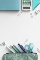 Top view of white desk with stationery. Office accessories in blue green colors. Creative concept with back to school. Vertical flat lay of supplies and copy space. photo