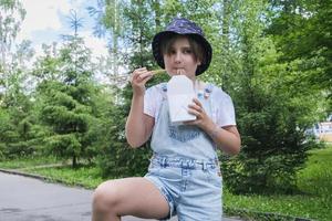 a teenage girl on a walk on a summer day in the park has lunch with noodles wok photo