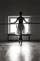 una bailarina encantadora en un traje de cuerpo posa elementos de ballet en un tocado en un estudio fotográfico foto