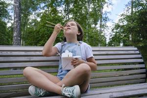 a teenage girl on a walk on a summer day in the park has lunch with noodles wok photo