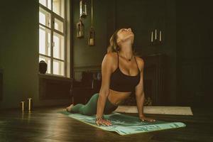 una chica encantadora con uniforme deportivo hace yoga en una habitación antigua con chimenea y velas foto