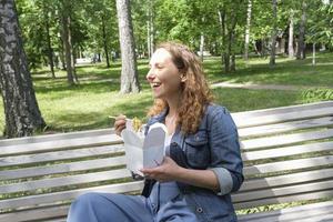 a mid adult mature woman on a walk on a summer day in the park has lunch with noodles wok photo