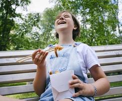a teenage girl on a walk on a summer day in the park has lunch with noodles wok photo