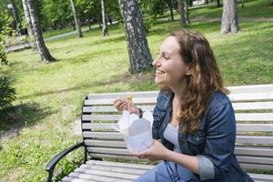 a mid adult mature woman on a walk on a summer day in the park has lunch with noodles wok photo