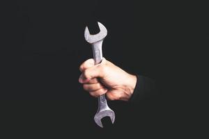 spanner tool in a man hand on black background - maintenance sercice concept photo