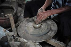 Selective focused on the dirty wrinkled skin hands of old man molding the clay work on the spinning wheel for making the traditional jar photo