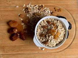 A bowl of oats with a few almonds and some dried fruits on a wooden base photo