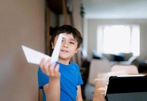 Happy school boy looking at camera with smiling face while showing origami Swan paper. Kid learning paper art origami lesson, Child having fun doing Art and Craft at home, Home schooling concept photo