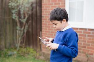 Happy Child boy holding tablet pc standing outside waiting for School bus, Portrait Kid playing game online or reading strory on internet, Preschool boy learning with modern technology photo