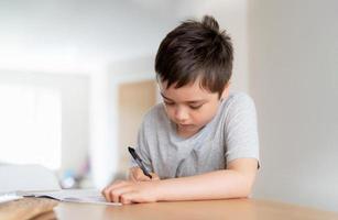 School kid using black pen drawing or writing the letter on paper, Young boy doing homework, Child with pen writing notes in paper sheet during the lesson.Cute pupil doing test, Homeschooling concept photo