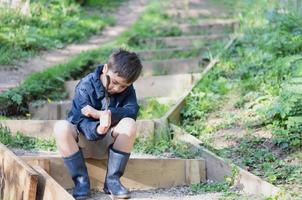 Happy young boy playing outdoor in the garden, Portrait Kid sitting on step holding wooden stick enjoy playing outside in the morning , Child relaxing on sunny day Spring or Summer in the park. photo