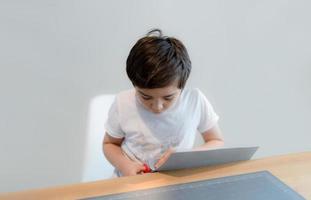 Kid using scissors cutting cardboard , Schoolboy making art and craft for his homework,Child learning how to use the scissors cut the paper,Children learn and play at home, Home school concept photo