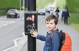 niño de la escuela presionando un botón en los semáforos en el paso de peatones de camino a la escuela. niño con mochila usando instalaciones peatonales controladas por semáforos para cruzar la calle. foto