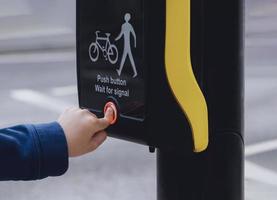 School kid finger pressing  button at traffic lights on pedestrian crossing on way to school. People using traffic signal controlled pedestrian facilities for crossing road photo