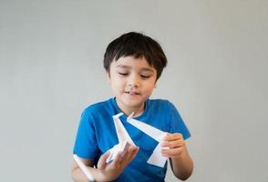 Happy school boy looking at origami Swan paper on his hands. Kid learning paper art origami lesson, Child having fun doing Art and Craft at home, Home schooling concept photo
