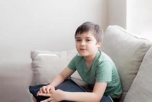 retrato de un niño usando una tableta jugando en Internet con un amigo, un niño educado en casa haciendo la tarea en línea con una libreta digital en casa, un niño sentado en un sofá mirando la cámara con una cara sonriente. foto