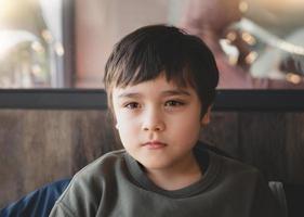 Cinematic portraitPortrait Kid looking deep in thought,Dramatic Young boy sitting alone in coffee shop or cafe waiting for food, A Child looking out with thinking face. photo