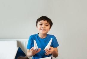 Happy school boy looking at camera with smiling face while showing origami Swan paper. Kid learning paper art origami lesson, Child having fun doing Art and Craft at home, Home schooling concept photo