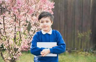 Happy young boy holding tablet pc standing outside waiting for School bus, Portrait  Kid with smiling face standing alone in the front garden, Preschool boy learning with modern technology photo