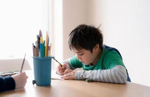 niño feliz usando dibujo a lápiz de color o esbozando en papel, niño retratado sentado en la mesa haciendo la tarea, niño disfruta del arte y la actividad artesanal con amigos, concepto de educación foto