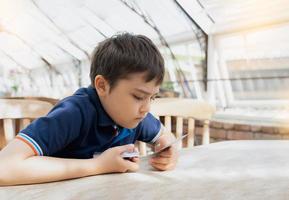 Young boy playing card game in the cafe while waiting for food, Kid with curious face looking at paper card on his hands,  Family playing board game indoor on sunny day spring or Summer. photo
