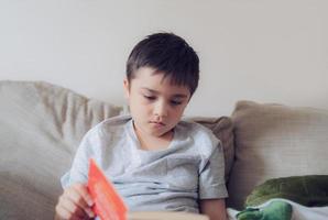 niño de la escuela de retrato leyendo un libro para la tarea, niño sentado en el sofá disfruta leyendo la historia en la sala de estar, niño relajándose en casa el fin de semana. concepto de educación o educación en el hogar foto