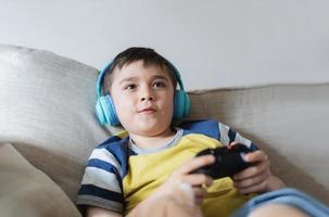 Portrait kid wearing headphones and playing video game. Child holding console play game online with friends at home, Young boy siting sofa having fun and relaxing on his own on weekend photo