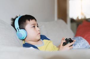 niño de retrato usando auriculares y jugando videojuegos. niño sosteniendo un juego de consola en línea con amigos en casa, un niño sentado en un sofá divirtiéndose y relajándose solo el fin de semana foto