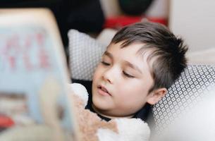 Closeup face School kid reading a book for homework,Head shot Young boy lying on sofa enjoy reading the story in living room,Child relaxing at home on sunny day Spring,Home Schooling,Education concept photo