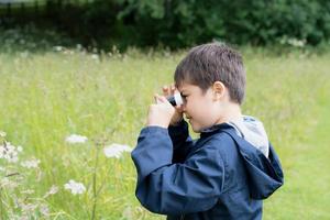 Kid looking through mini microscope with wondering face, Excited Child on a camping school trip in green forest, Kid explorer with wildlife nature in summer camp, Travel and Education concept photo