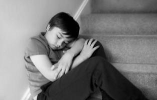 Black and White portrait Sad boy sitting alone on staircase, Lonely kid looking dow with sad face not happy to go back to school, Depressed child boy sitting in the corner of a stair,Mental health photo