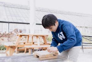 Smart kid building wooden blocks on table in the garden.Young boy playing  and creating a tower or building a house construction,Happy child doing outdoor activity in sunny day Spring or Summer photo