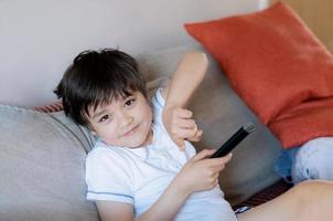 Young boy holding remote control and looking at camera with smiling face, Happy kid relaxing at home in the morning photo
