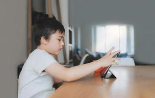 niño jugando en línea con amigos en tableta, retrato cinematográfico joven videollamada con amigos mientras desayuna, niño viendo dibujos animados en Internet, niño de la escuela haciendo la tarea en la libreta digital foto