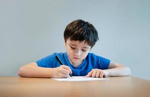 School kid using black pen drawing or writing the letter on paper, Young boy doing homework, Child with pen writing notes in paper sheet during the lesson.Cute pupil doing test, Homeschooling concept photo