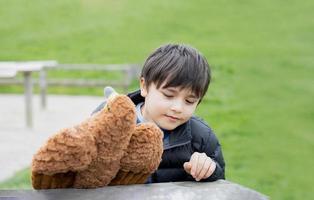 niño feliz sentado en un banco jugando con un juguete de pájaro en el parque en la mañana soleada, niño jugando en los campos de primavera, niño positivo con cara sonriente relajándose o divirtiéndose en actividades al aire libre. foto