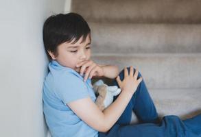 Sad School kid sitting alone on staircase in the morning, Lonely boy looking dow with sad face not happy to go back to school, Depressed child boy sitting in the corner of a stair,Mental health photo