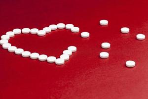 comprimidos de medicamentos médicos apilados sobre un fondo rojo en forma de corazón foto