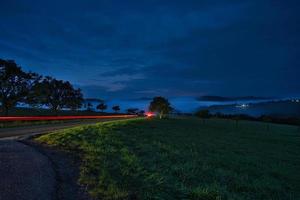 road with trees and meadows at blue hour in the evening photo
