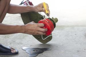 las manos del mecánico están actualizando una cortadora de césped de la cuchilla para instalar una cuerda para cortar el césped. foto