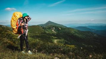 Woman tourist is walking on a hiking trail with a backpack against background of green mountains and sky photo